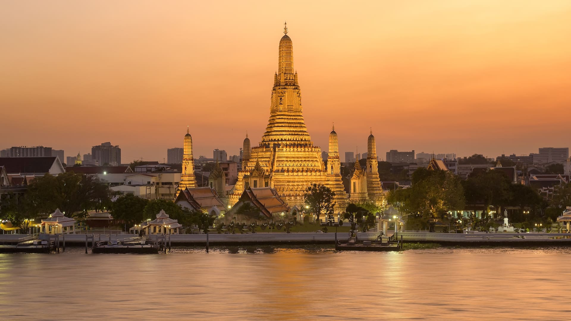 Wat Arun Temple of Dawn illuminated at sunset along the Chao Phraya River, one of the most iconic places to visit in Bangkok with family